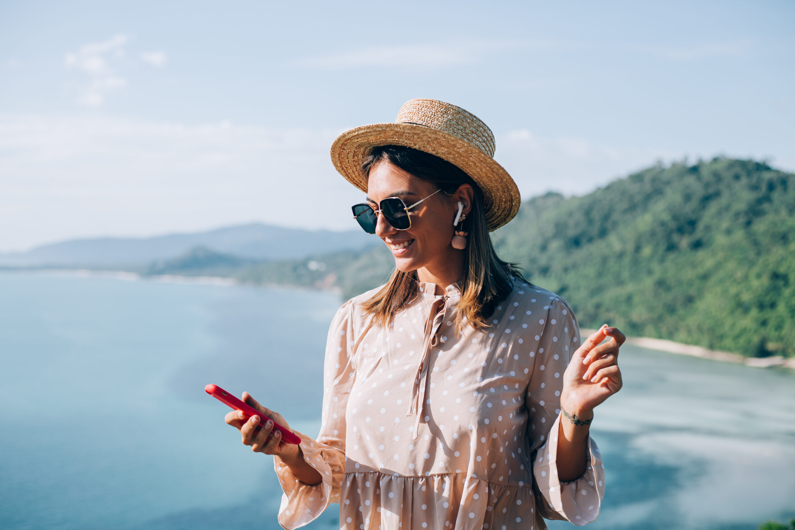 young woman in summer cute dress straw hat and sunglasses dancing with smartphone on hand and listening to music scaled