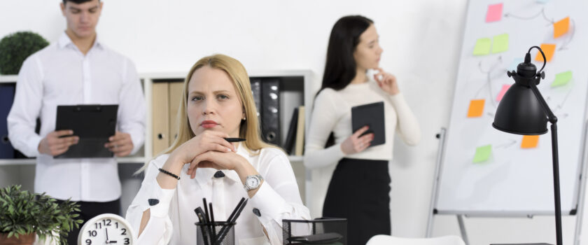 colleague standing behind the serious young businesswoman at workplace