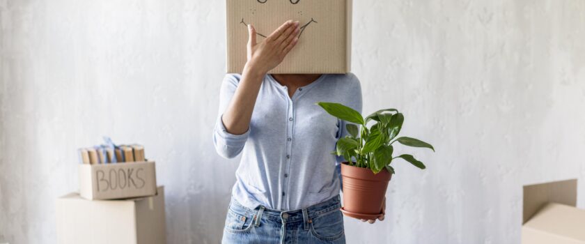 silly woman posing with box over head and plant in hand while packing to move