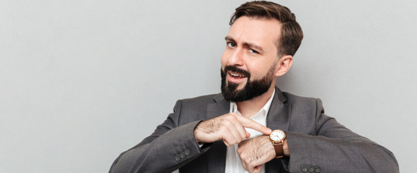 horizontal bearded man pointing his wrist watch posing isolated gray