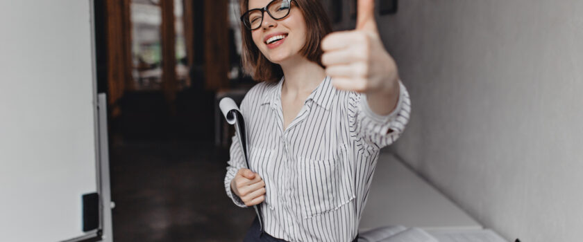 shot charming business woman glasses showing thumbs up posing with huge amount papers office